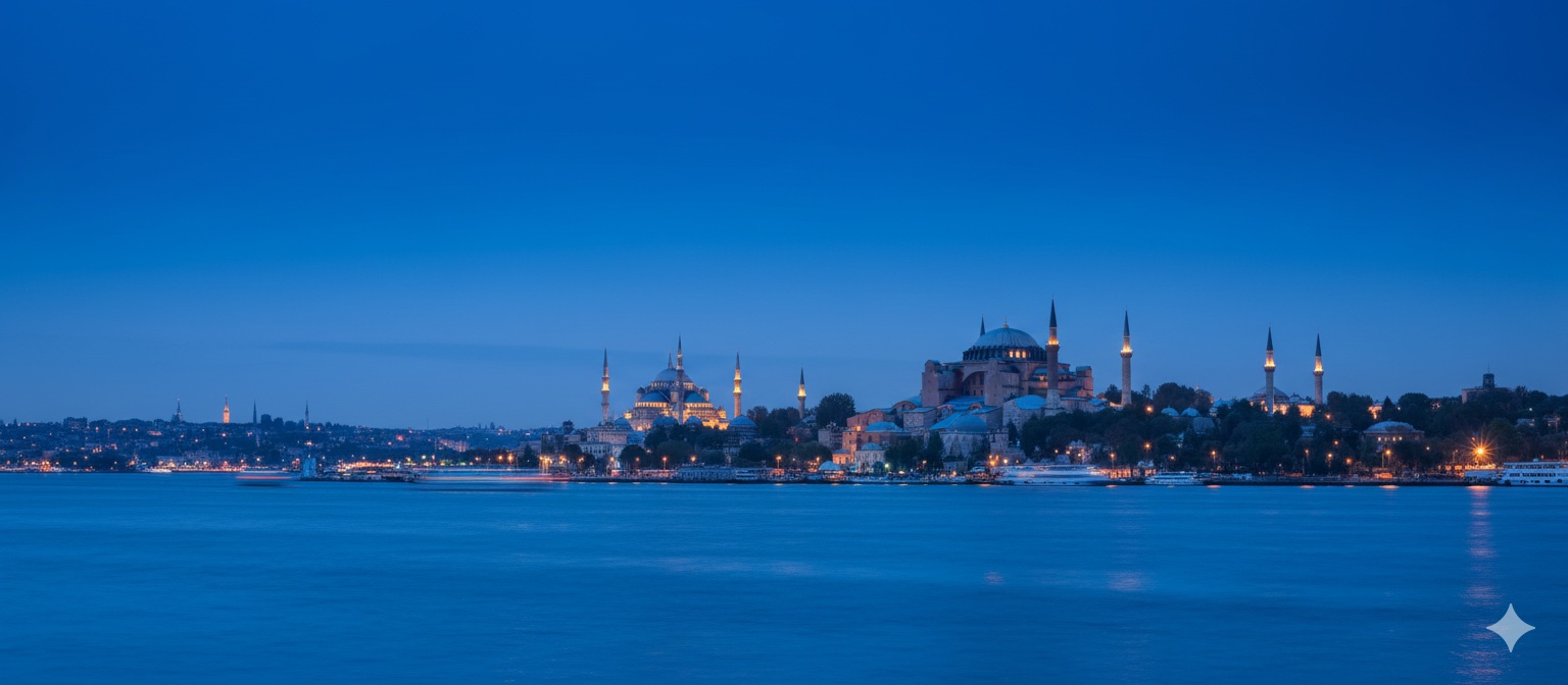 İstanbul'un simgesel Ayasofya ve Sultan Ahmet Camii'nin alacakaranlıkta aydınlatılmış, ön planda şehir ışıklarını yansıtan Boğaz'ın derin mavi gökyüzü altındaki çok geniş panoramik görünümü.